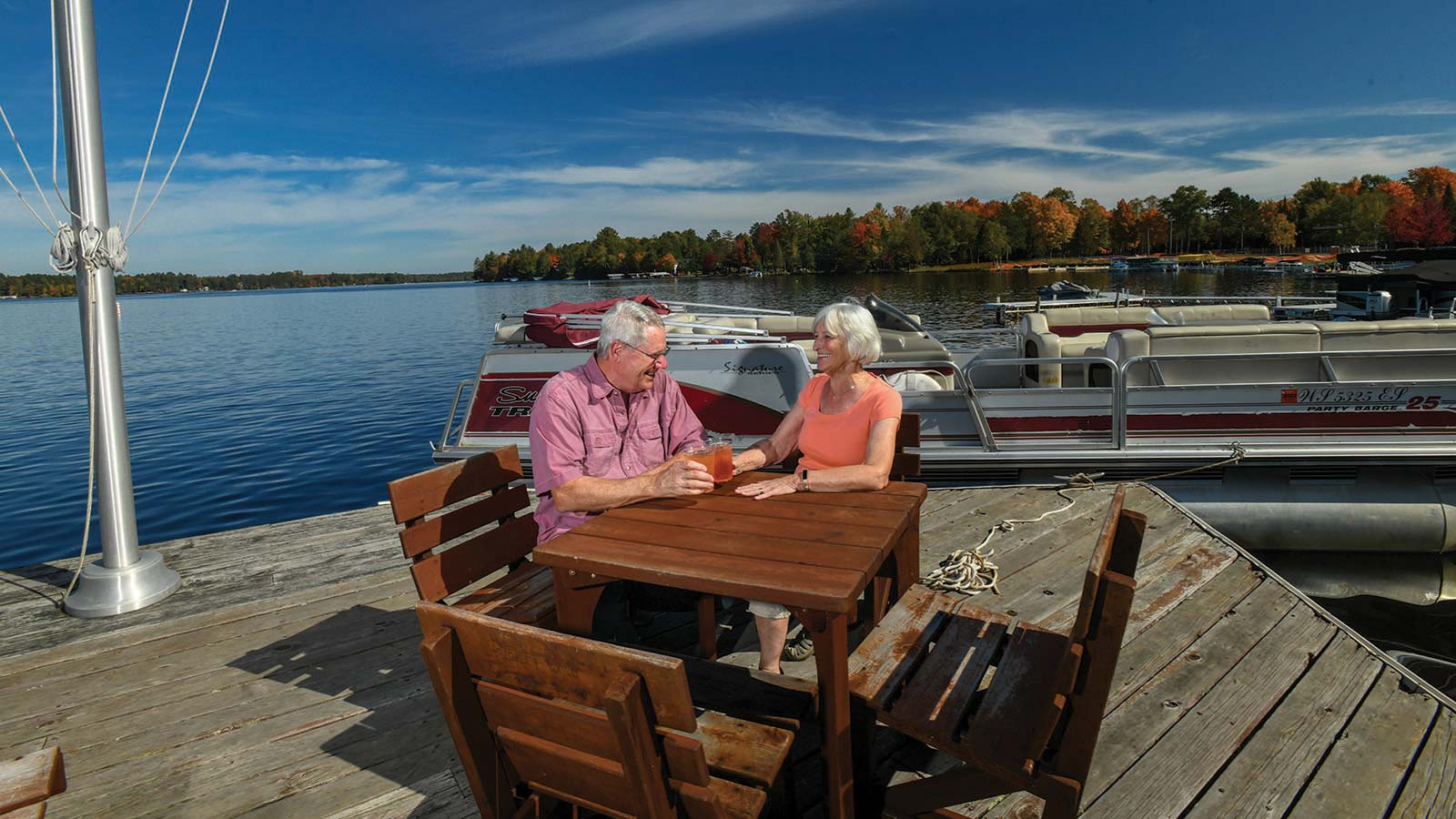 Couple enjoying drinks on the dock next to their pontoon in fall time