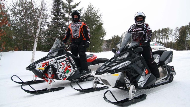 Adventure North Snowmobile Tours and Rentals | Snowmobiliers standing on their sleds on the trail