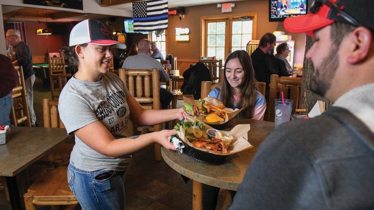 Cross Country Bar & Grill | Waitress serving brugers and fries to a family at Cross Country Bar and Grill