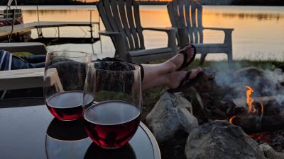 Two empty chairs and glasses of wine on a dock at sunset
