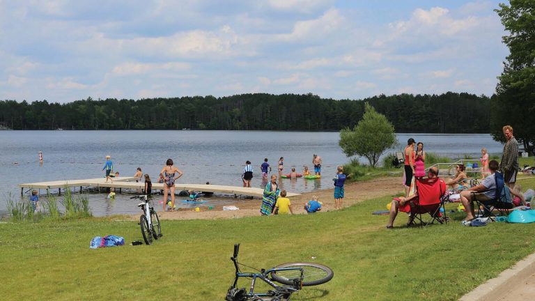 People enjoying the public beach with a dock in the summertime