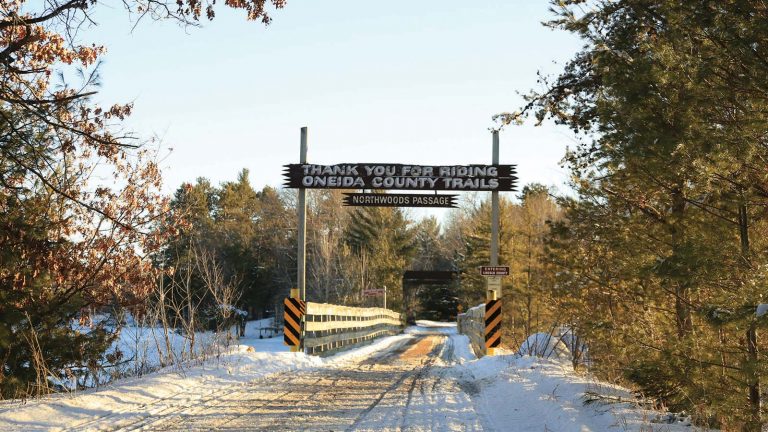 Related Article: Oneida County snowmobiling guide | Northwoods Passage sign above a bridge on the snow covered Hiawatha and Bearskin trail