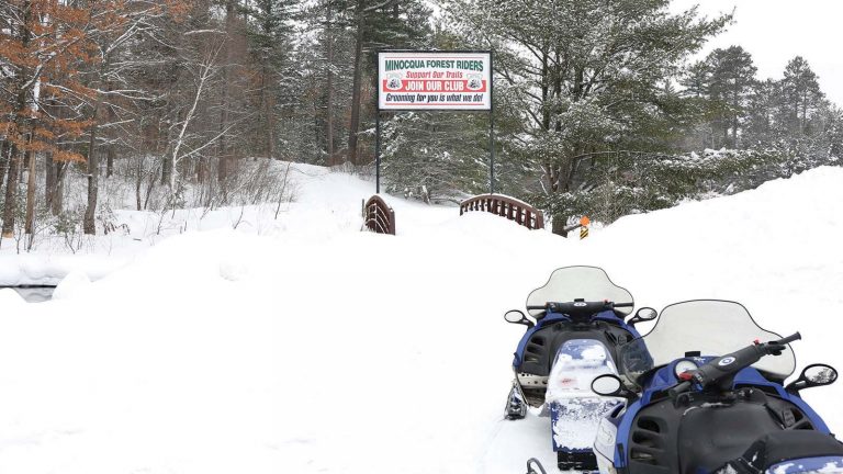 Related Article: Oneida County: A snowmobiler’s paradise | Two snowmobiles on front of a Minocqua Forest Riders trail sign on the snow covered trail