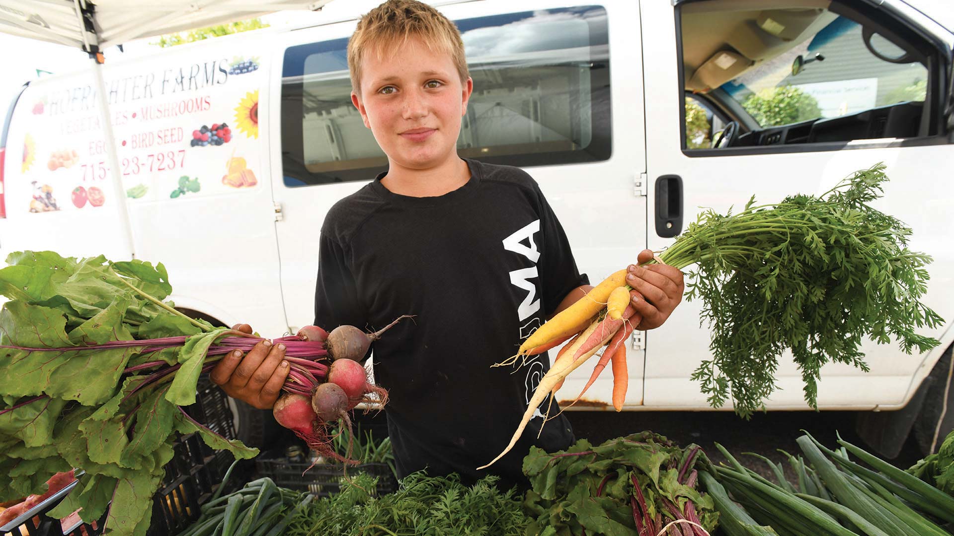 Kid holding up fresh-grown produce at the farmers market