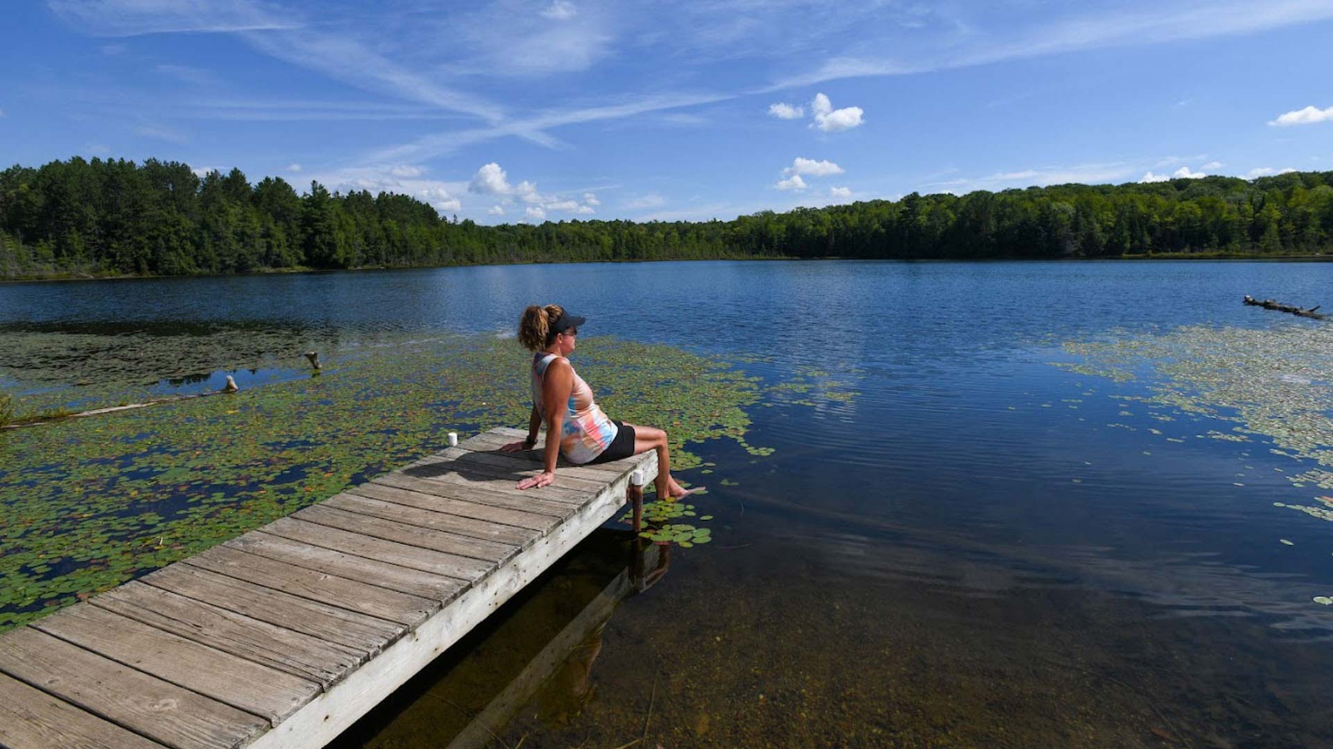 Visit Oneida County This Summer | Women sitting on a dock with her feet in the water at Eagle LAke