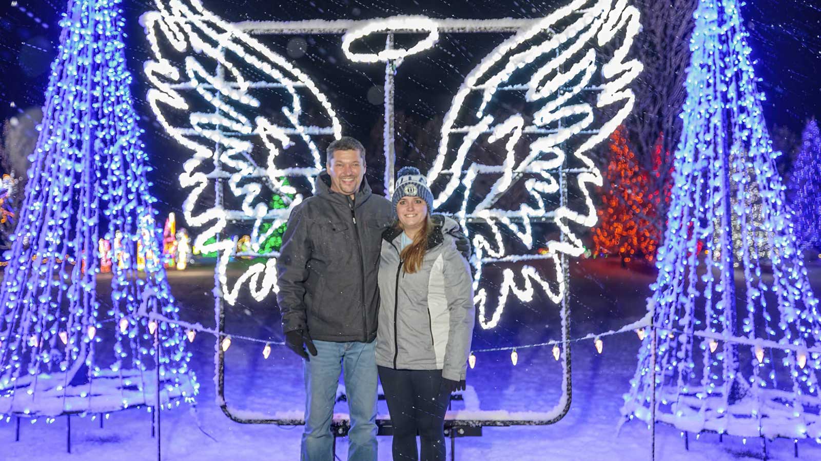 Catch these stunning holiday light shows this winter | Couple posing in front of angel wings light display at A Christmas Wonderland holiday light show in Harshaw in Oneida County Wisconsin