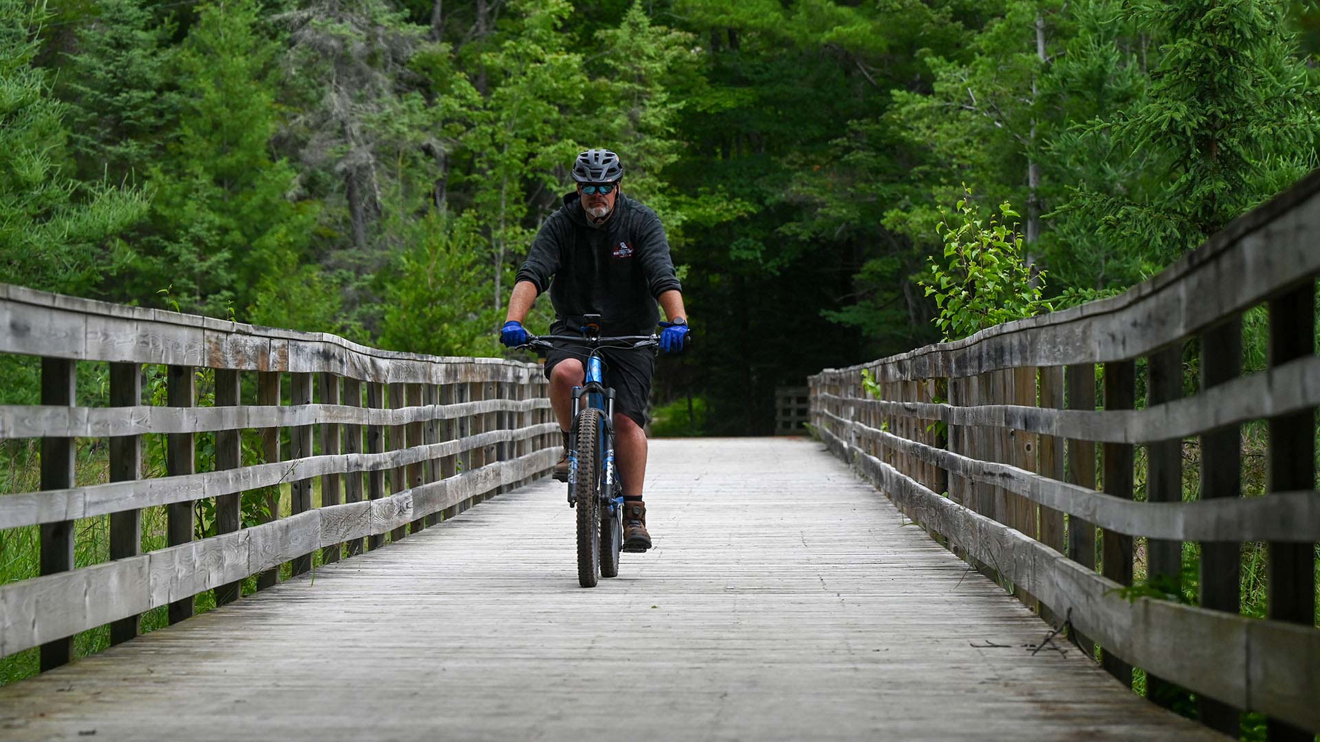 Plan Your Summer Vacation to Oneida County | Man biking over the wood bridge on Three Eagle Trail