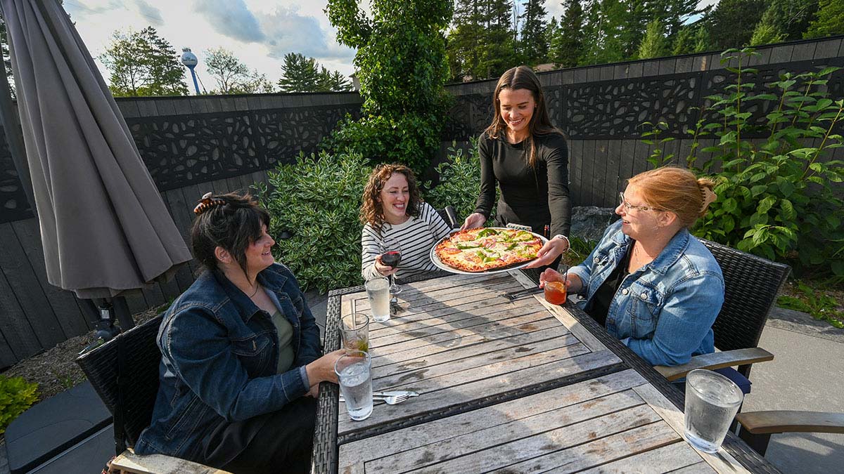 Plan Your Summer Vacation to Oneida County | Pizza being served to a group of women sitting on the outdoor patio at Claytons 1881 Room